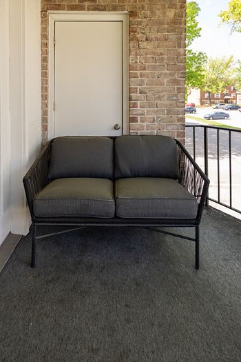 A black sofa with a metal frame is placed in a room with a white door and a brick wall at The Brittany Apartments, Pikesville, MD